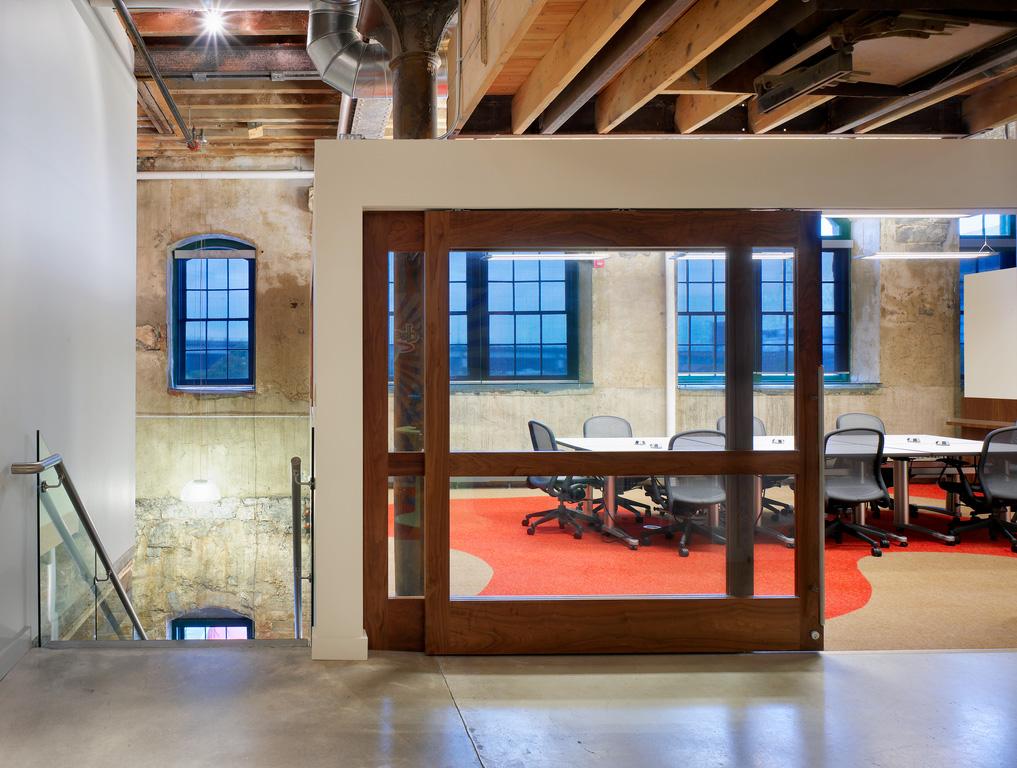 A boardroom with sliding glass doors framed in wood, in a converted heritage factory building with concrete floors, exposed stone walls and exposed wood ceiling