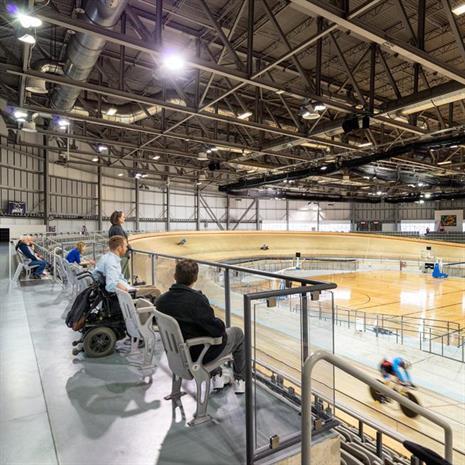 people with varying mobility needs watch from accessible viewing stands as cyclists ride a wooden track 