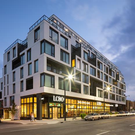 a white midrise condominium building with cube-like balconies and windows in a random pattern, with an LCBO on the ground floor