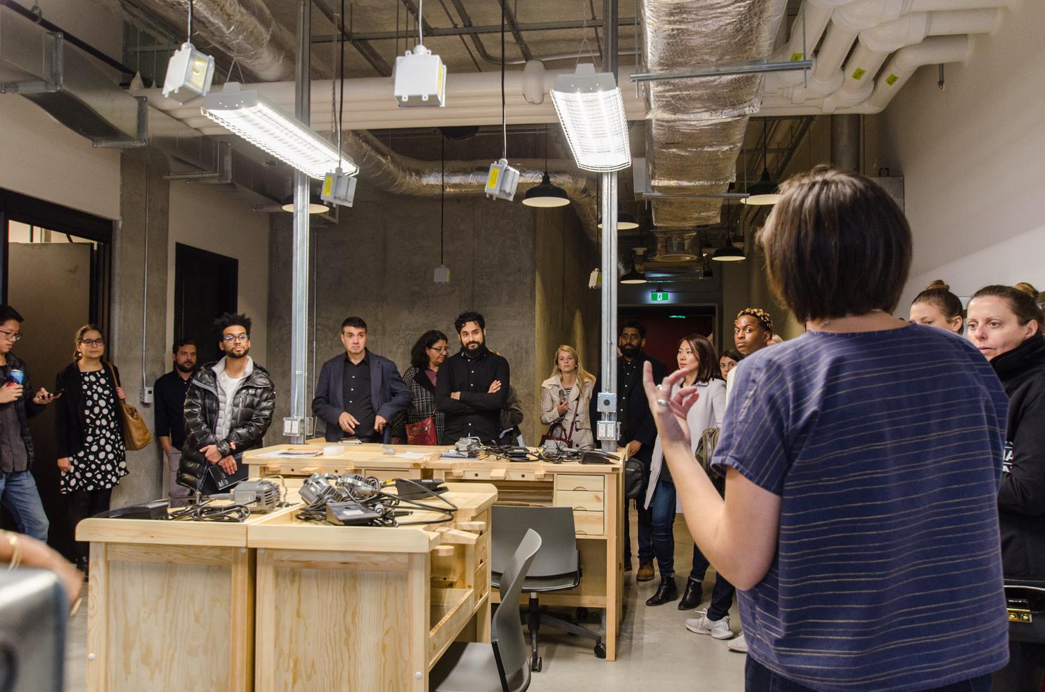 Tor McGlade leading an interior design tour of Artscape Daniels Launchpad, showing the group a prototyping workshop with wooden work stations