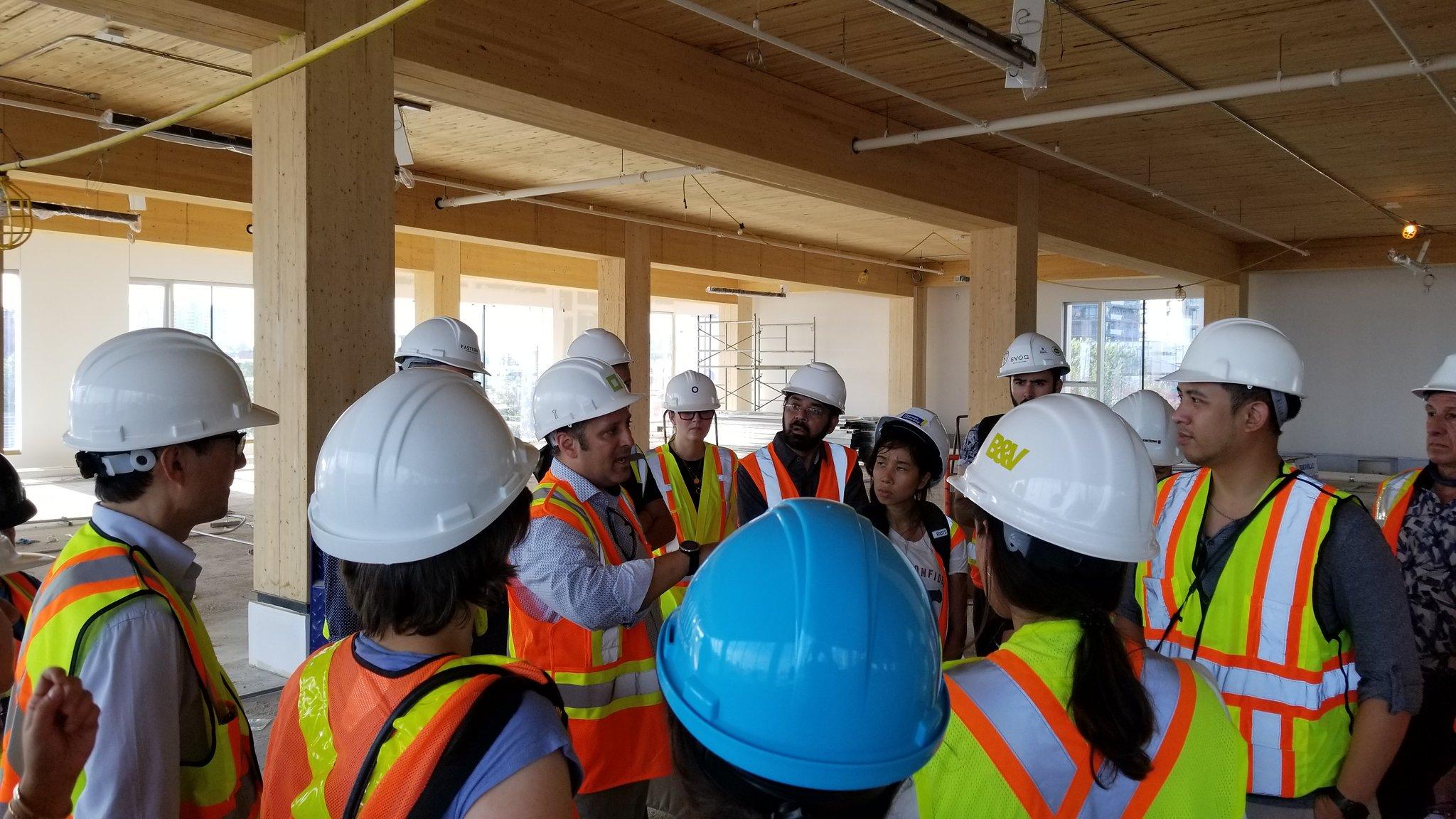 Richard Witt explaining something to a group of people wearing construction site safety gear in an unfinished floor of 80 Atlantic that features exposed wood ceilings and columns