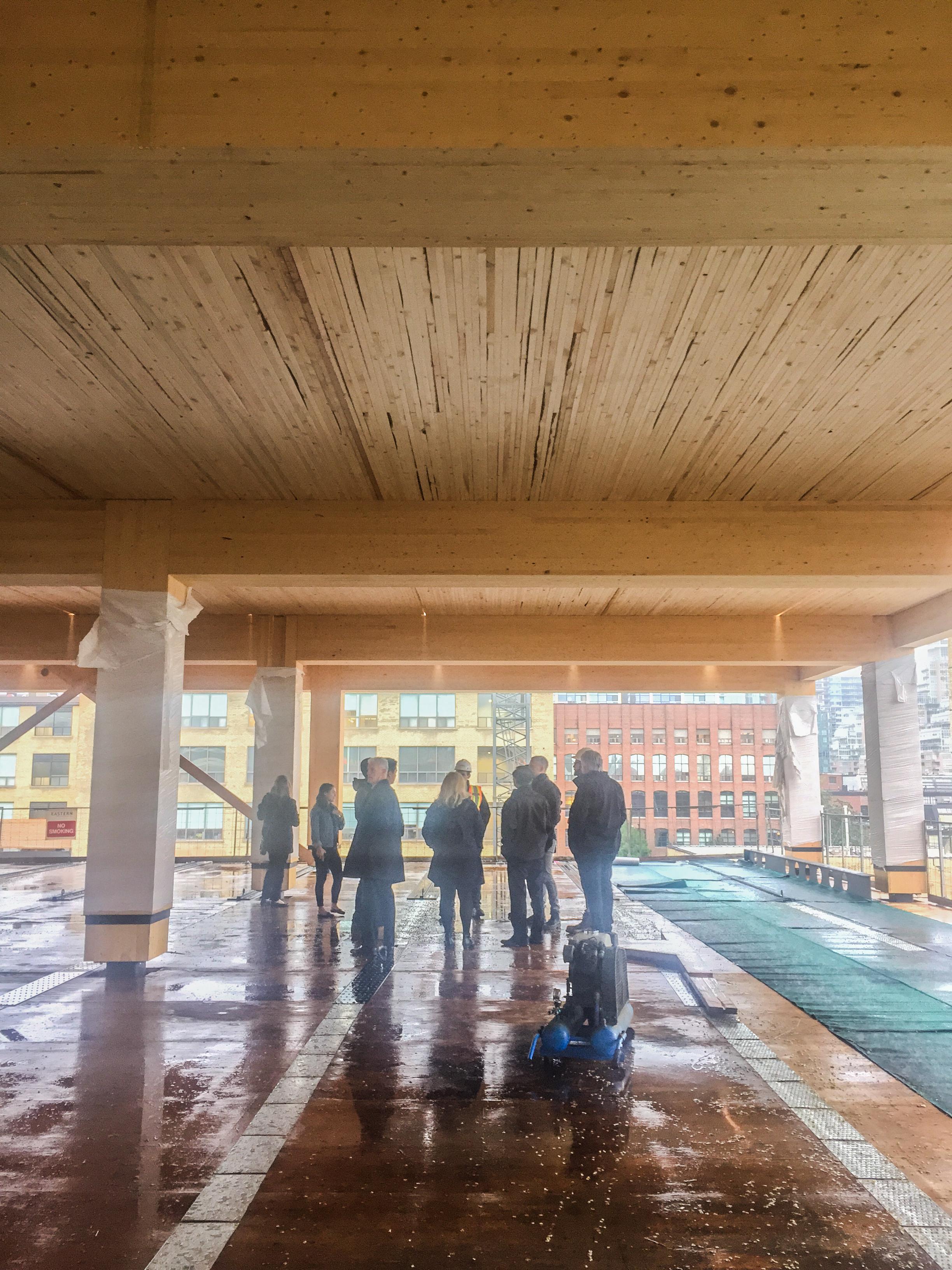 a group of people standing in the under construction 80 Atlantic looking at the wood post and beams and NLT deck timber ceiling