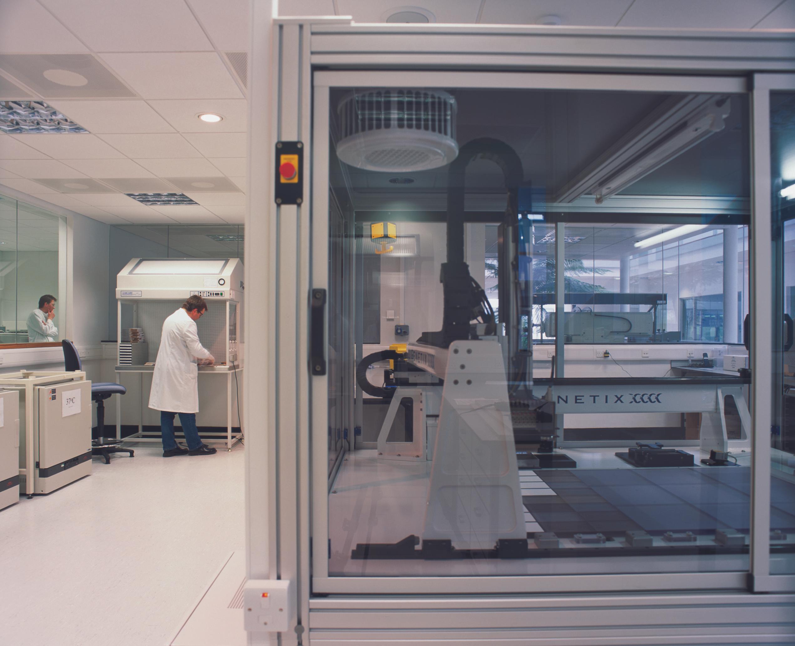 scientists in lab coats working beside a glazed specialized lab equipment room for testing genomes
