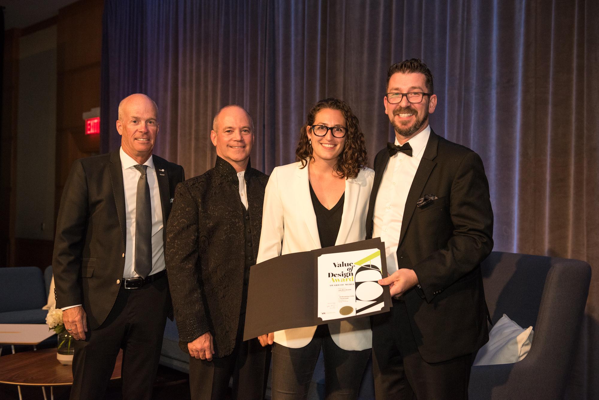 Quadrangle Associate Julie Mroczkowski posing for a photo with three men in suits, accepting a Value of Design Awards certificate