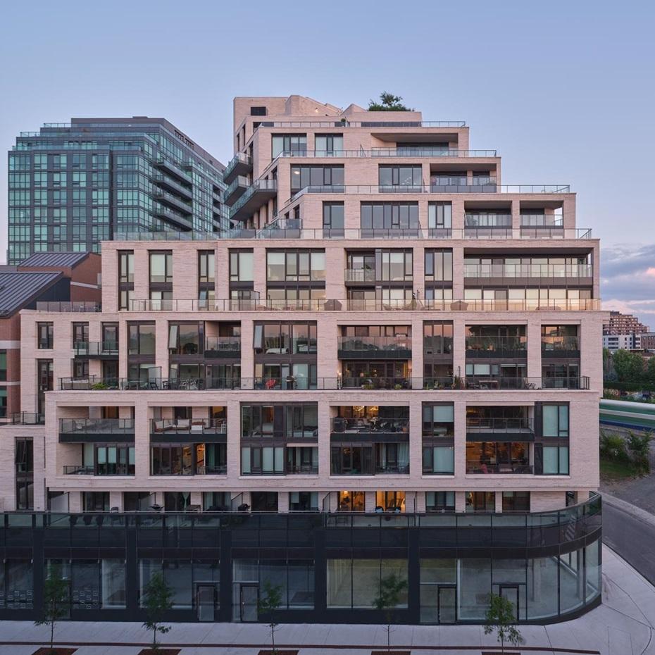 Rendering of a mid-rise condo building with a glass facade retail podium, white brick, and balconies that step back with each elevation.