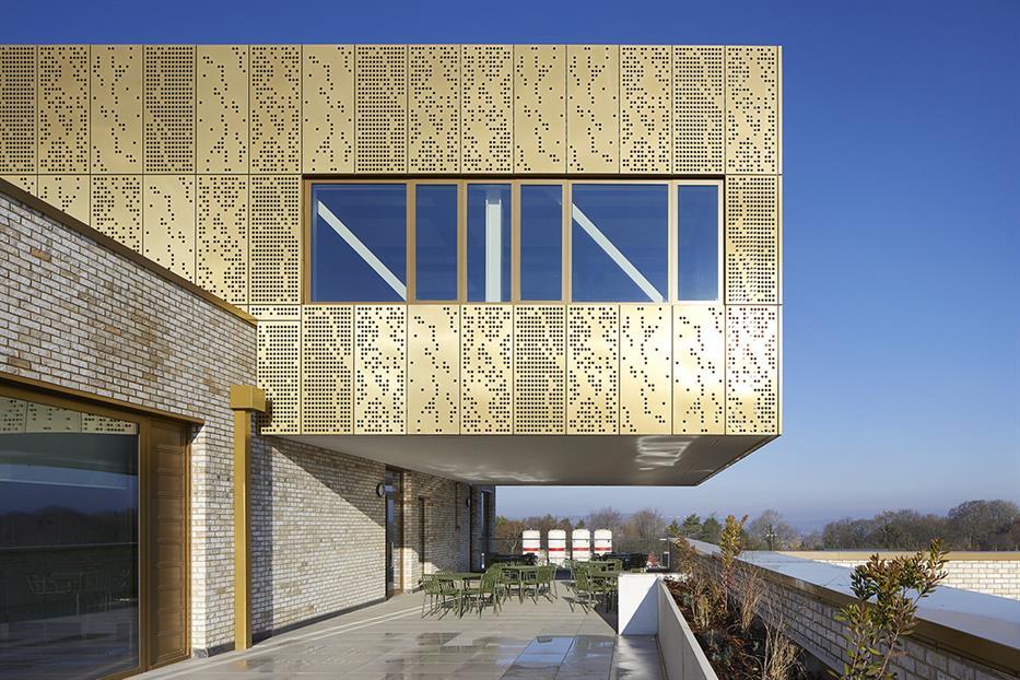 copper alloy perforated facade portion of Mulberry Park Community Hub shown to be cantilevered over an outdoor terrace with cafe seating