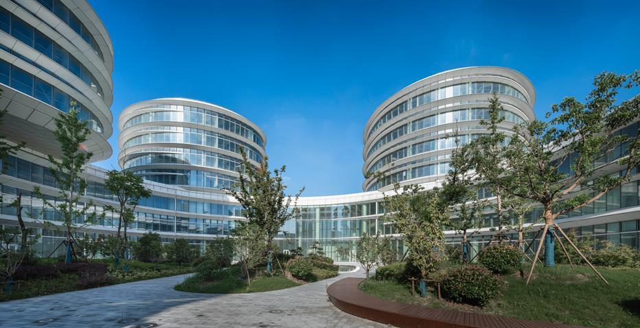 a courtyard with trees and landscaping, looking up at four-storey high towers connected by a curving glazed podium that encircles the courtyard